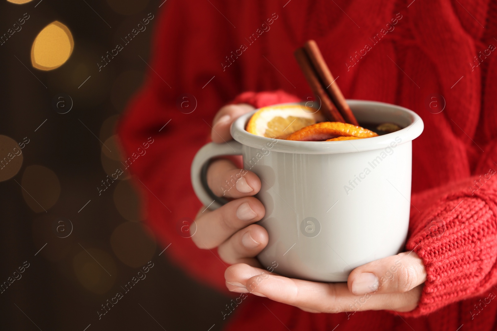 Photo of Woman holding cup of tasty mulled wine on blurred background