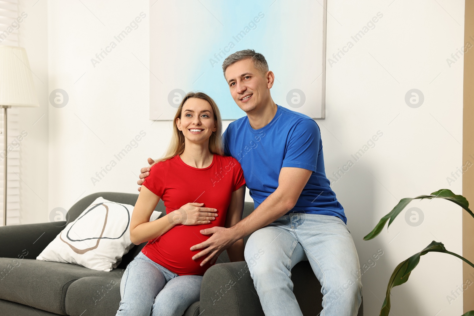 Photo of Young family housing concept. Pregnant woman with her husband on sofa at home