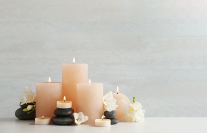 Beautiful composition with candles, stones and flowers on table against light background. Space for text