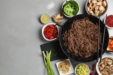 Wok with noodles, chicken and other products on light grey table, flat lay. Space for text