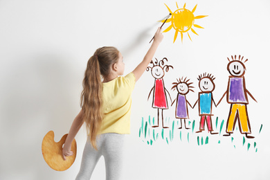 Little child drawing happy family on white wall indoors