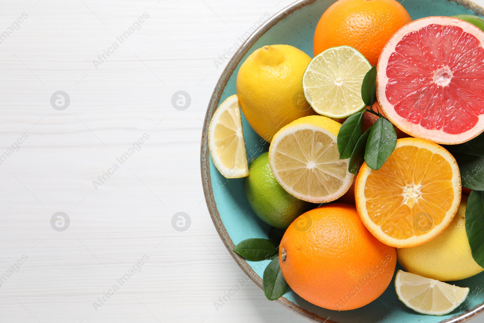 Photo of Different cut and whole citrus fruits on white wooden table, top view. Space for text