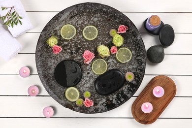 Photo of Plate with water, flowers, lime slices and burning candles on white wooden floor, flat lay. Pedicure procedure