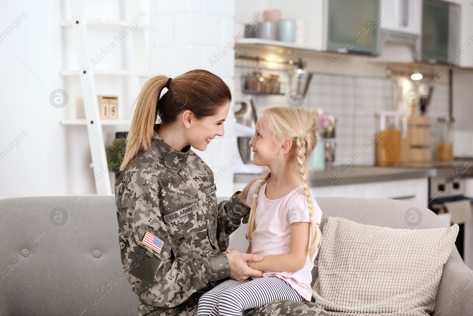 Photo of Woman in military uniform with her little daughter  on sofa at home