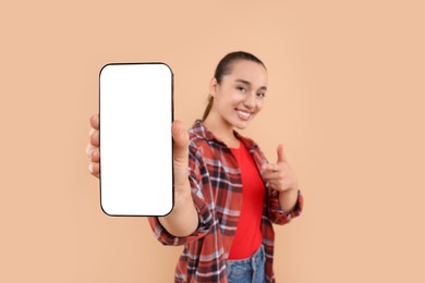 Young woman showing smartphone in hand and pointing at it on light brown background, selective focus. Mockup for design