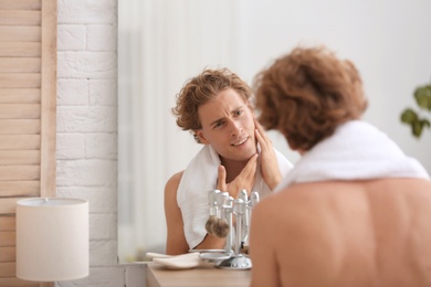 Young man looking in mirror after shaving at home