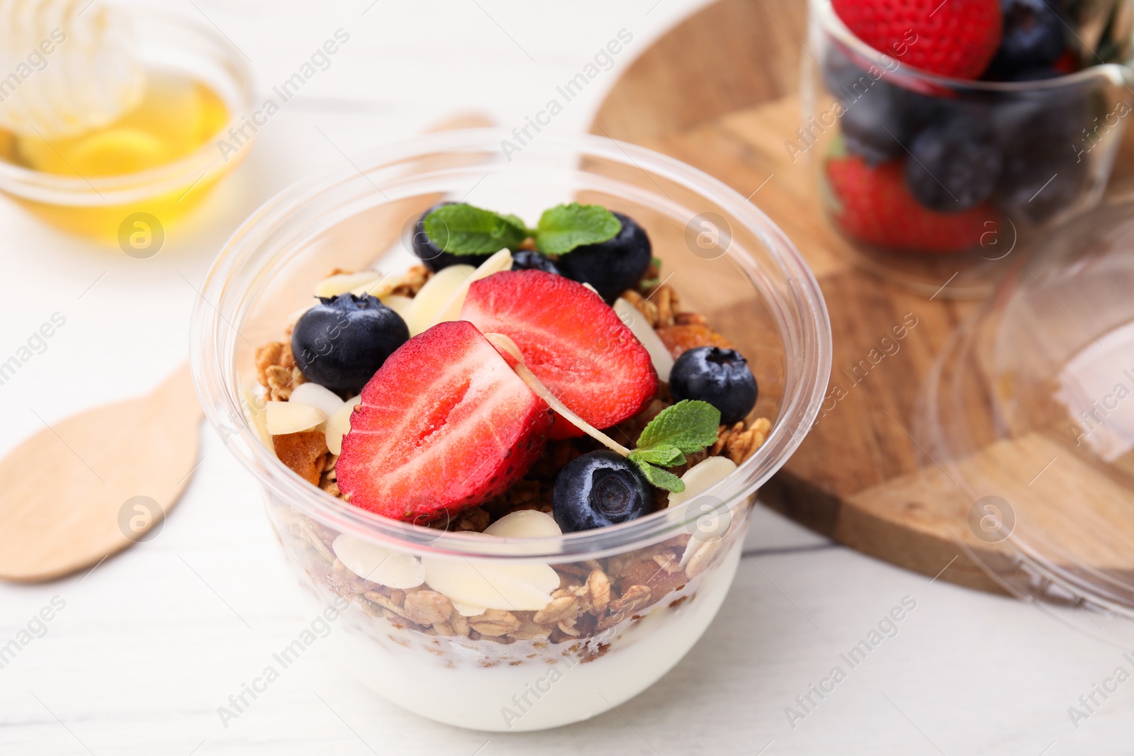 Photo of Tasty granola with berries, yogurt and almond flakes in plastic cup on white table, closeup