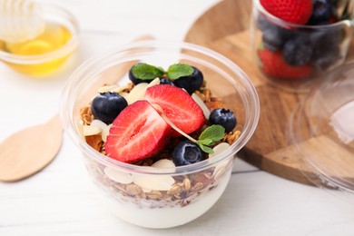 Photo of Tasty granola with berries, yogurt and almond flakes in plastic cup on white table, closeup