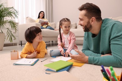 Photo of Father playing with his children while mother reading book on sofa in living room