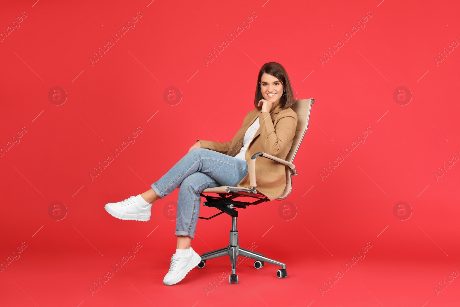 Photo of Young woman sitting in comfortable office chair on red background