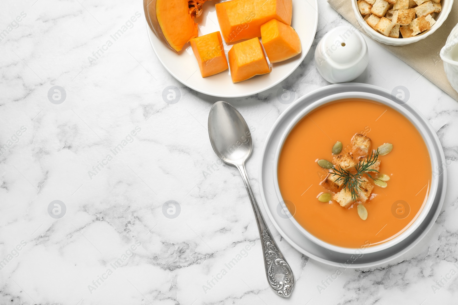 Photo of Tasty creamy pumpkin soup with croutons, seeds and dill in bowl on white marble table, flat lay. Space for text