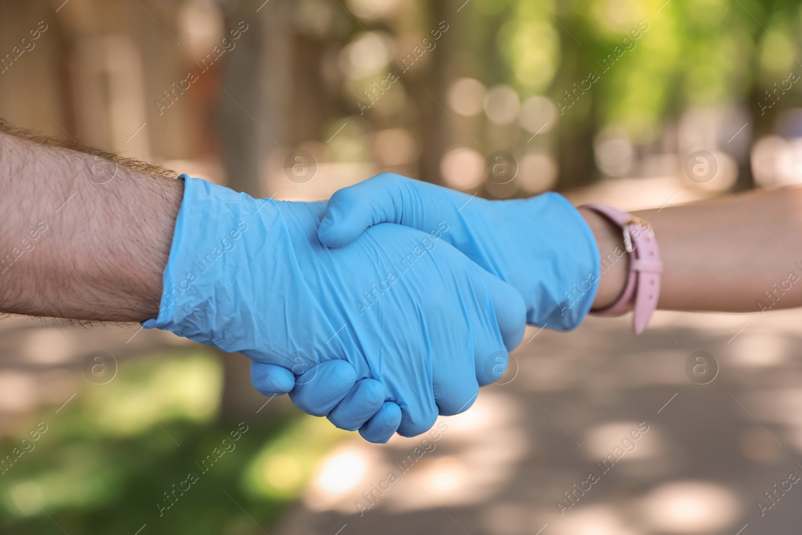 Photo of Man and woman in protective gloves shaking hands to say hello outdoors, closeup