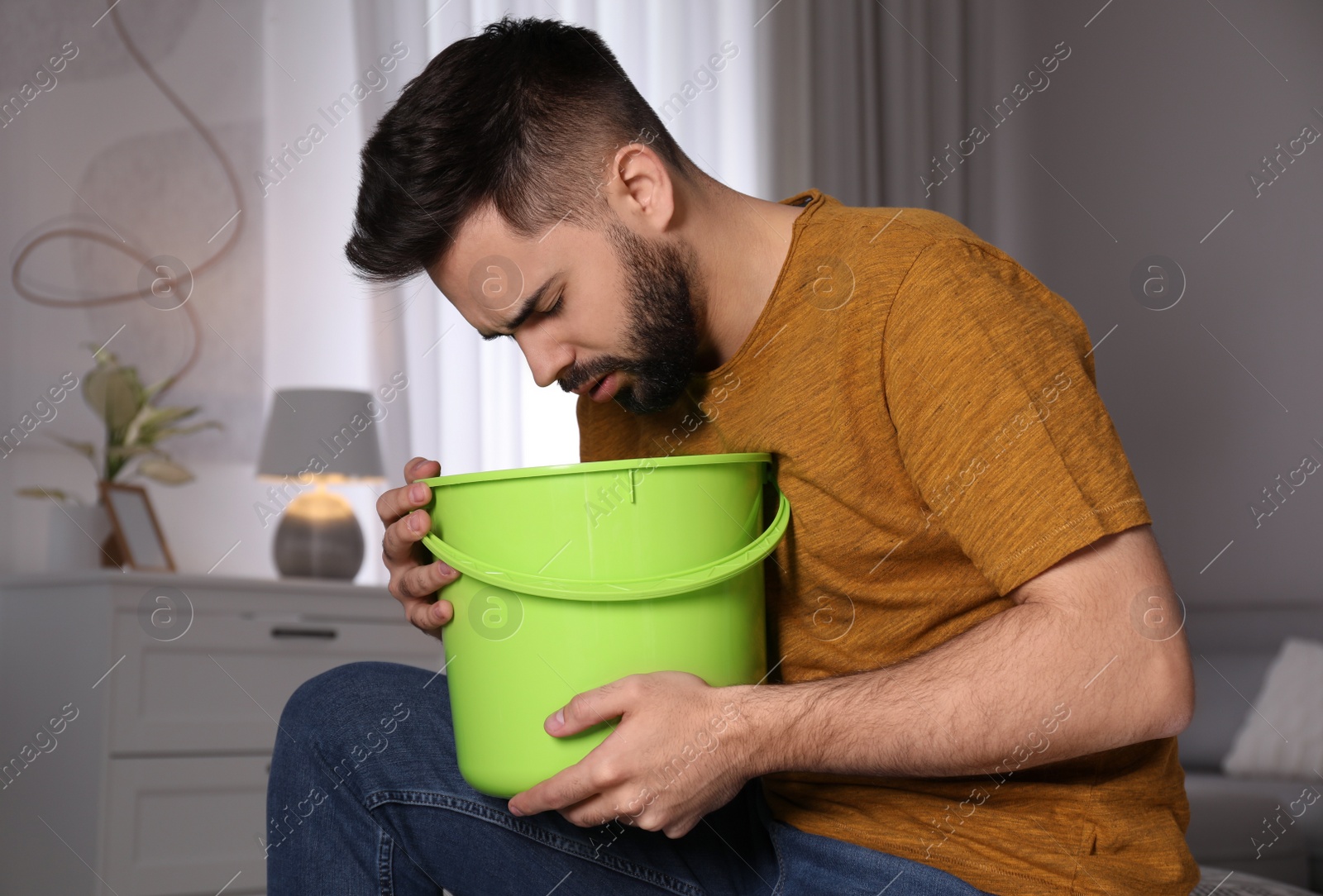 Photo of Young man with bucket suffering from nausea at home. Food poisoning