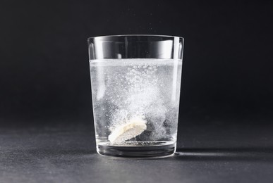 Effervescent pill dissolving in glass of water on grey table