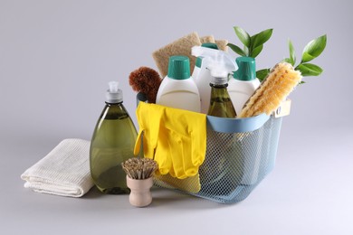 Set of different cleaning supplies in basket on light grey background