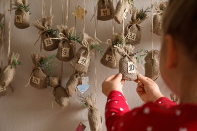 Little girl taking gift from New Year advent calendar indoors, closeup