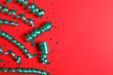 Photo of Turquoise serpentine streamers and confetti on red background, flat lay. Space for text