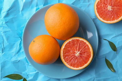 Plate with fresh yummy oranges on color paper  background