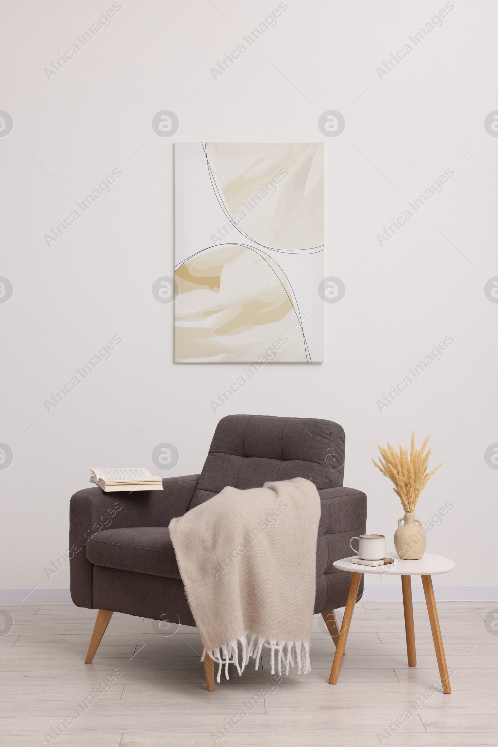 Photo of Comfortable armchair, blanket and side table near white wall indoors