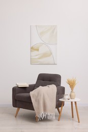 Photo of Comfortable armchair, blanket and side table near white wall indoors
