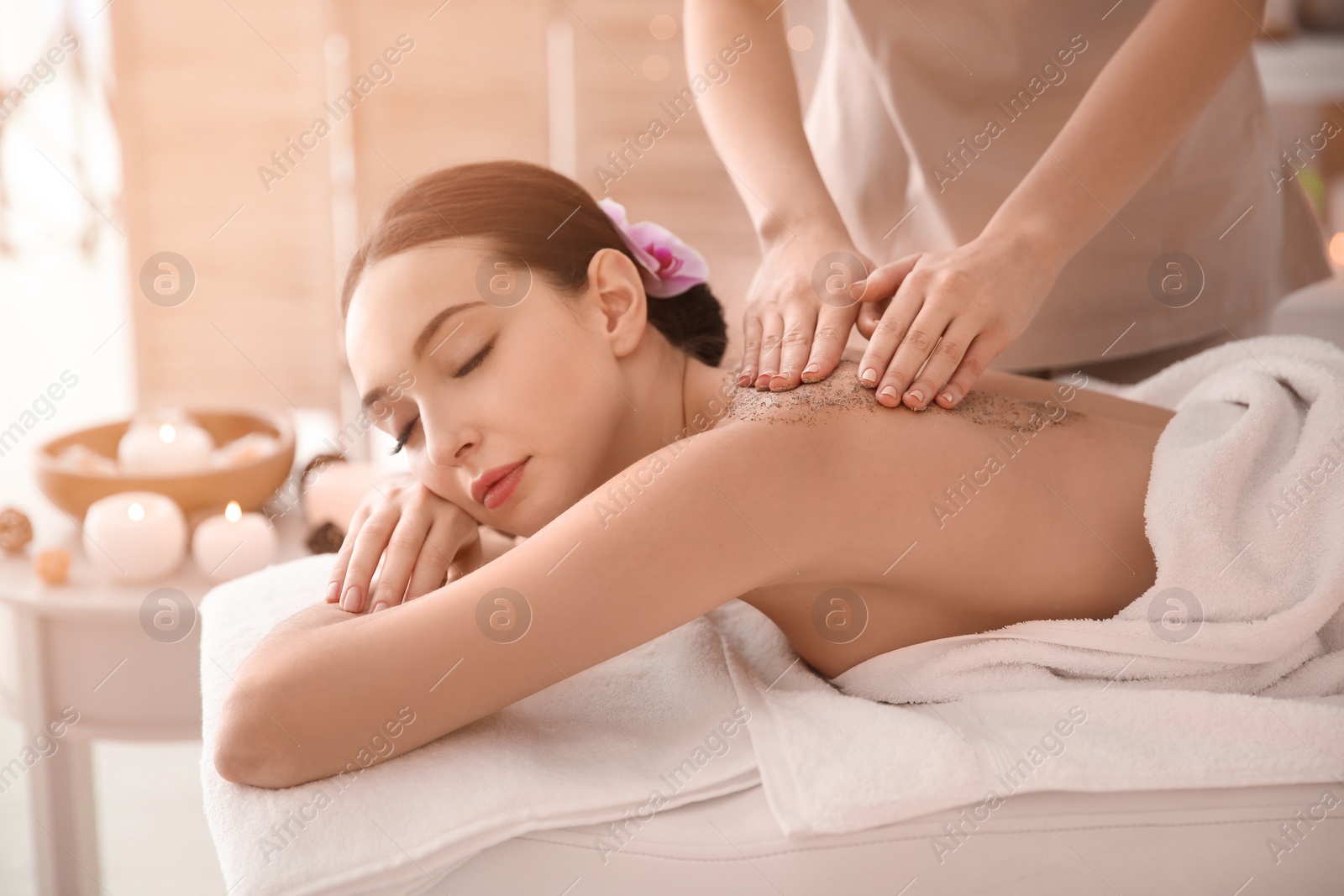 Photo of Beautiful young woman having massage with body scrub in spa salon