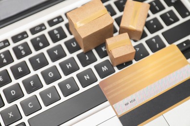Photo of Internet shopping. Small cardboard boxes and credit card on laptop, closeup. Space for text