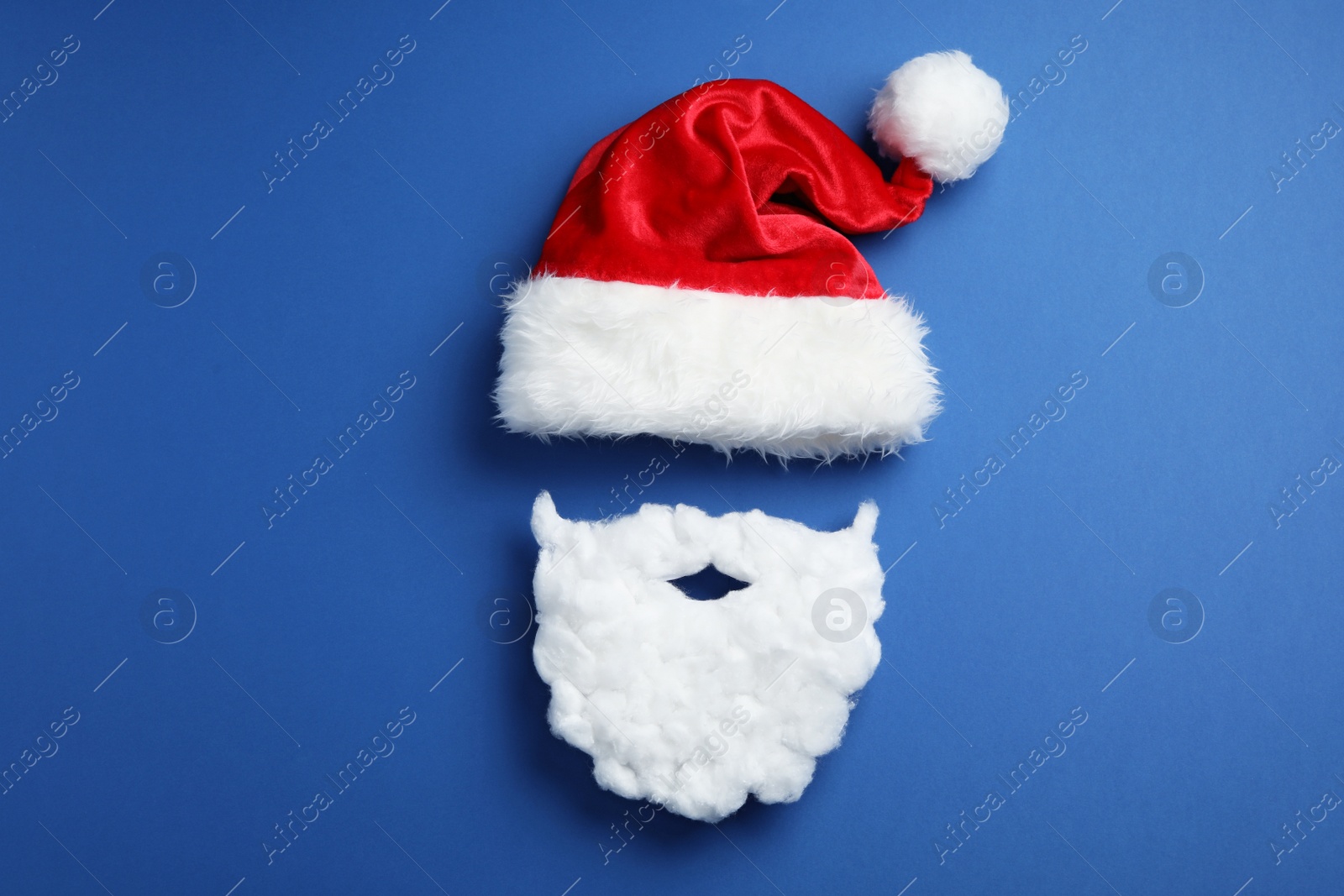 Photo of Santa Claus hat and beard on blue background, flat lay