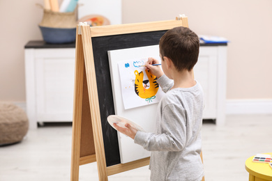 Little child painting on easel in room