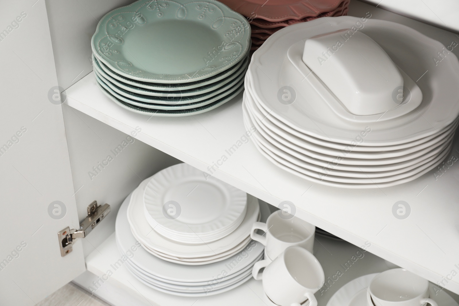 Photo of Clean plates, butter dish and cups on shelves in cabinet indoors