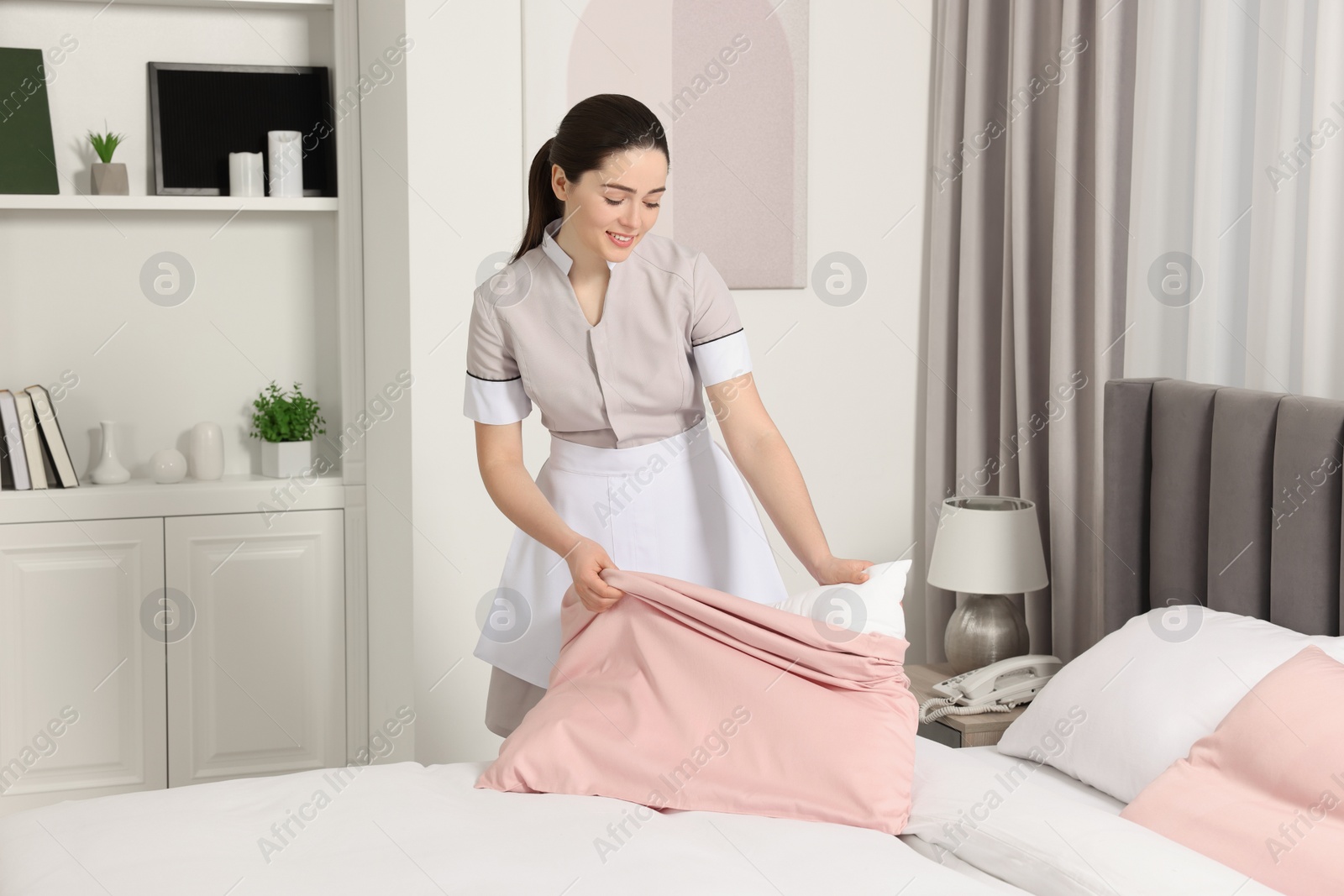 Photo of Young maid making bed in hotel room