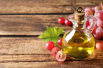 Photo of Jug of natural grape seed oil on wooden table, space for text. Organic cosmetic