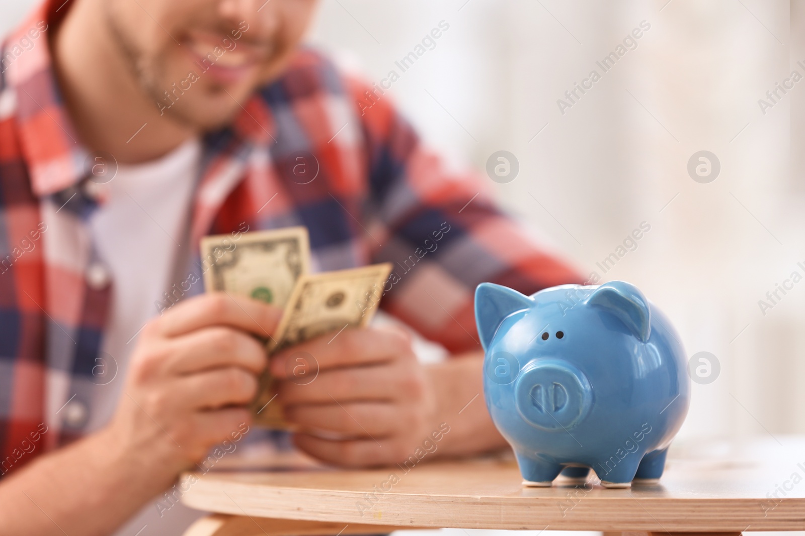 Photo of Man with piggy bank and money at home, closeup