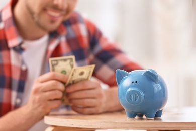 Photo of Man with piggy bank and money at home, closeup