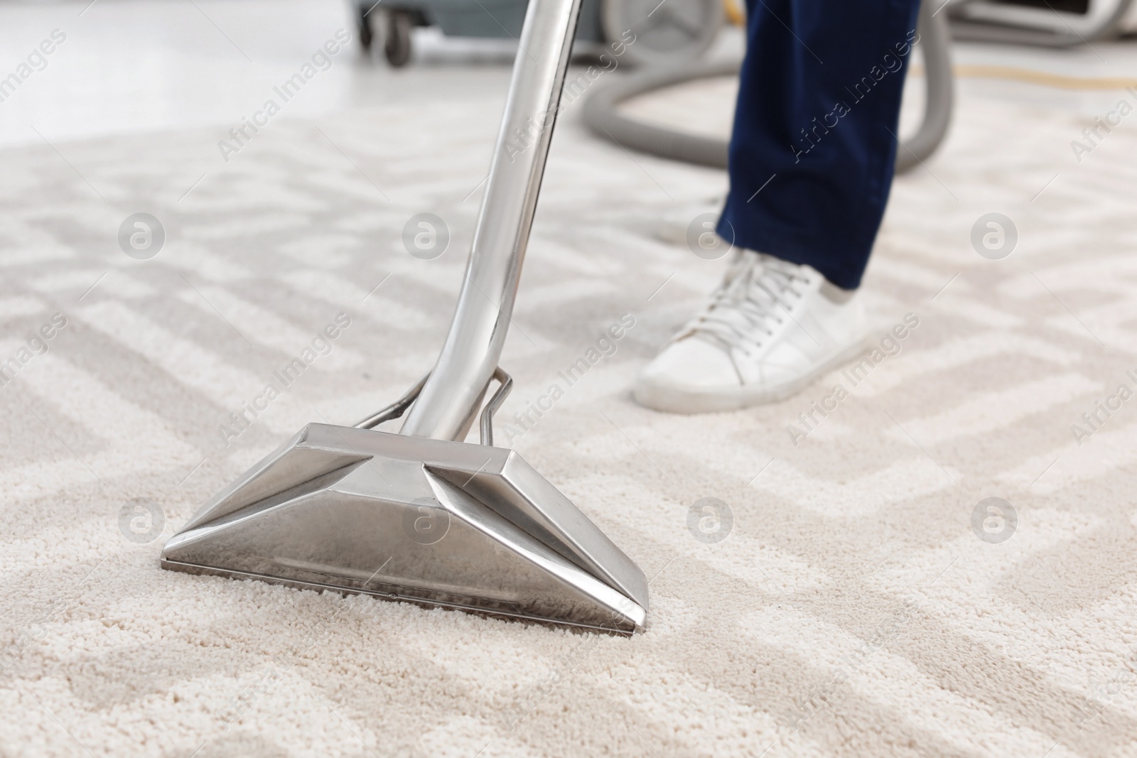 Photo of Male worker removing dirt from carpet with professional vacuum cleaner indoors