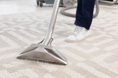 Male worker removing dirt from carpet with professional vacuum cleaner indoors