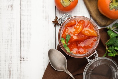 Photo of Jar of tasty persimmon jam and ingredients on white wooden table, flat lay. Space for text