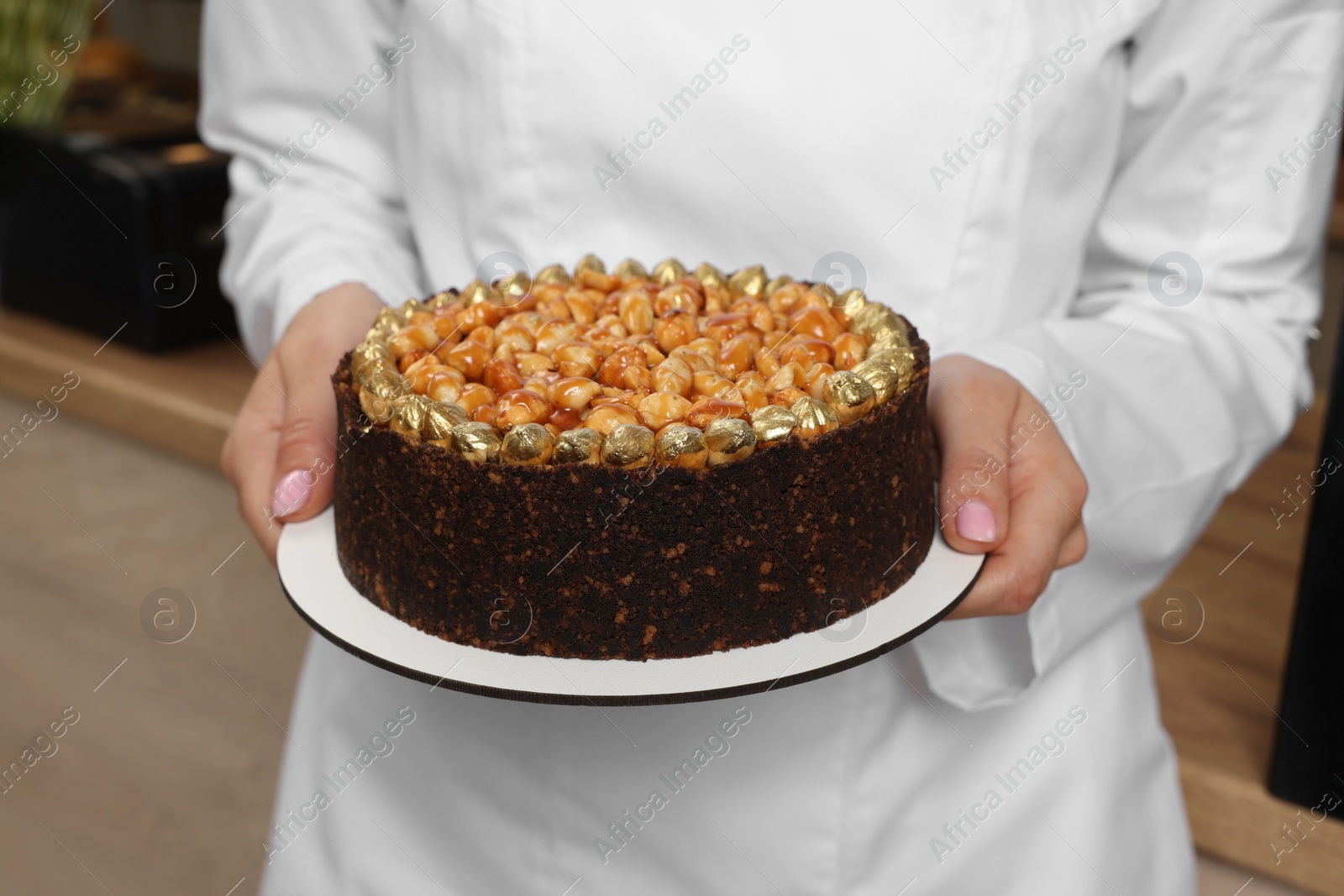 Photo of Baker holding delicious cake in cafe, closeup