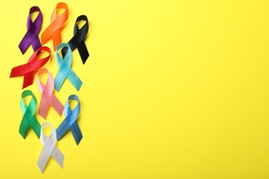 Colorful ribbons on yellow background, flat lay with space for text. World Cancer Day