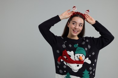 Photo of Happy young woman in Christmas sweater and Santa headband on grey background. Space for text