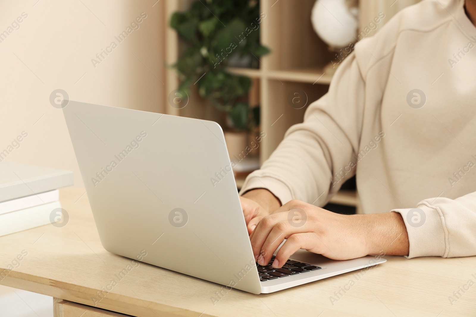 Photo of African American man typing on laptop at wooden table indoors, closeup