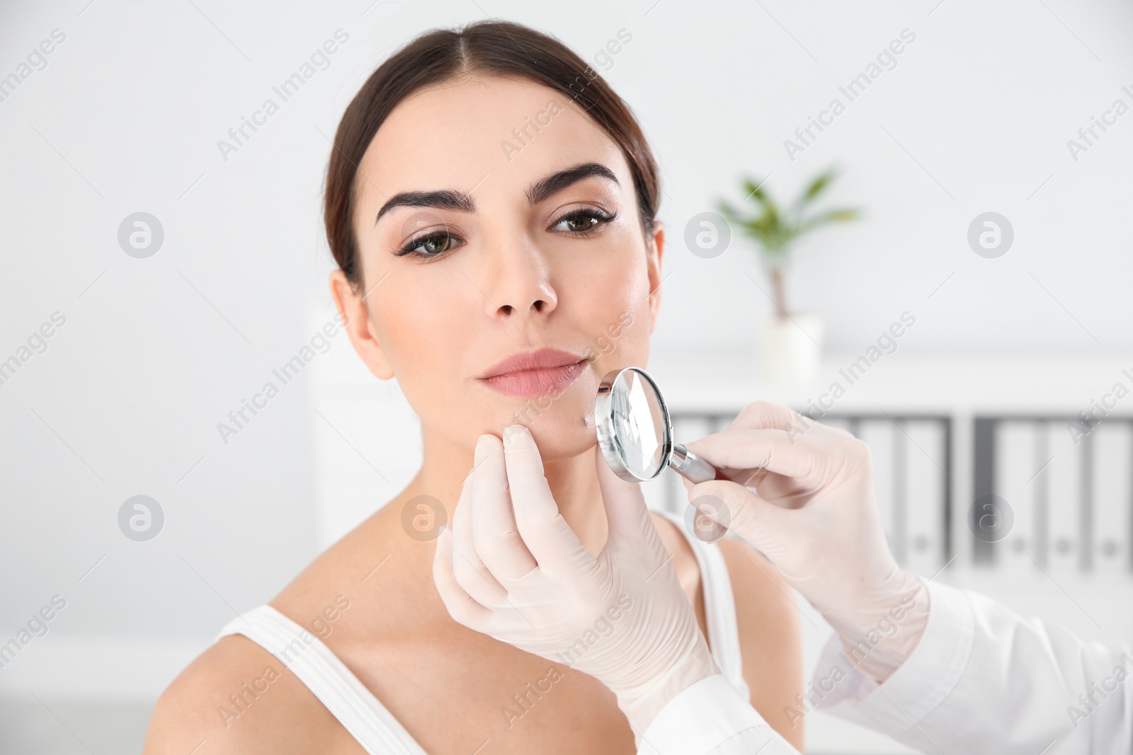 Photo of Dermatologist examining young patient's birthmark with magnifying glass in clinic