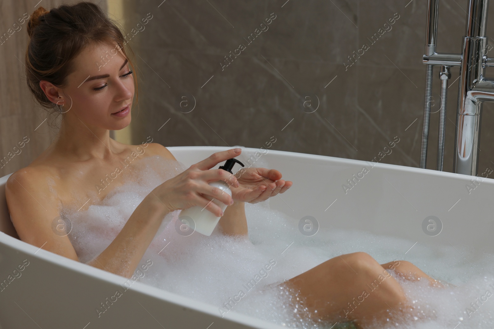 Photo of Beautiful woman pouring shower gel onto hand in bath indoors