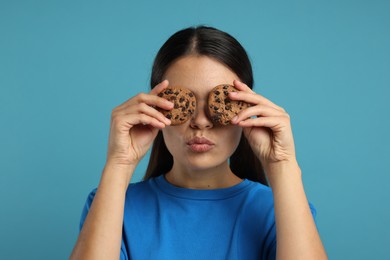 Photo of Young woman with chocolate chip cookies on light blue background