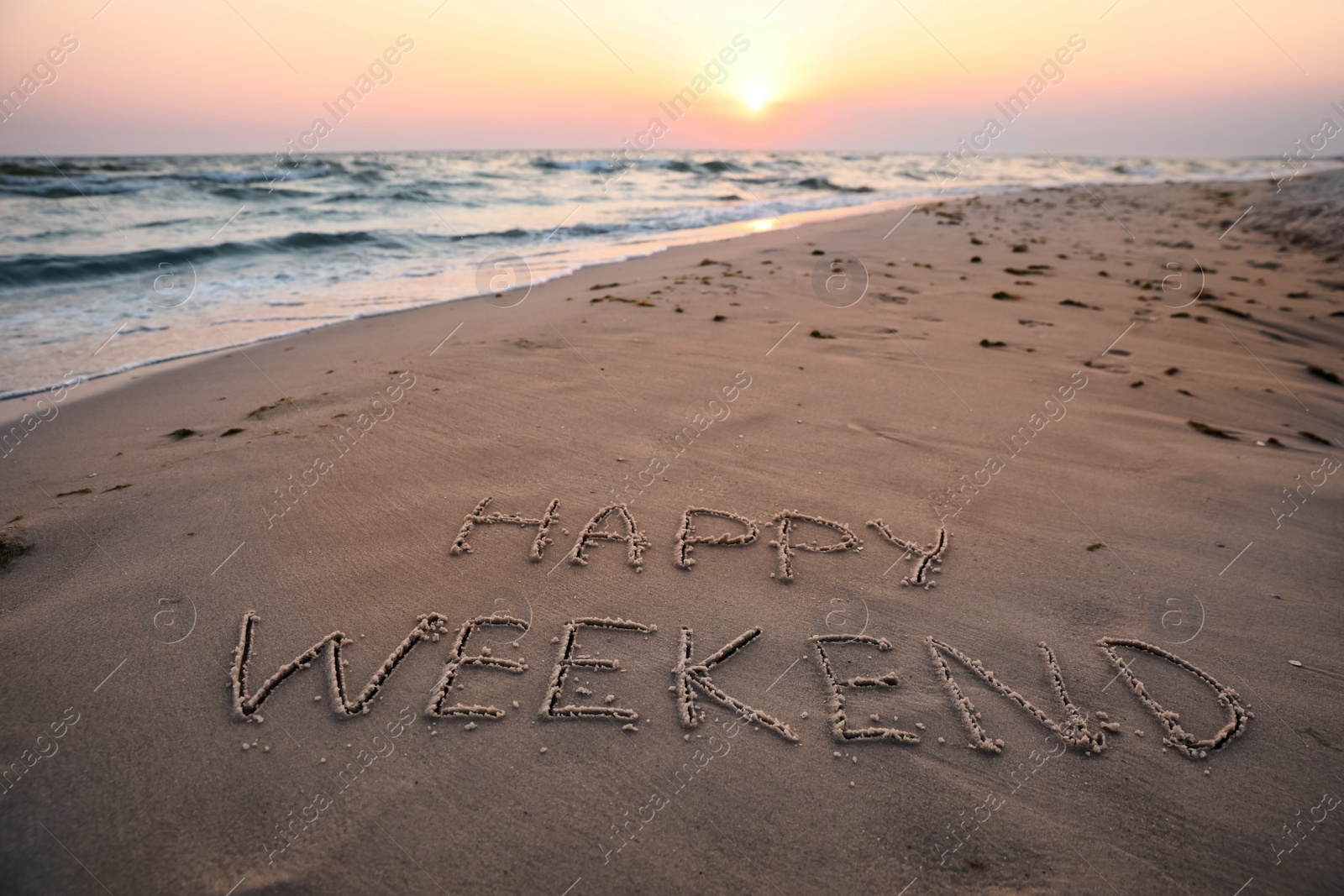 Photo of Text Happy Weekend written on sandy beach at sunset