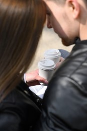 Lovely young couple with cups of coffee spending time together outdoors, closeup. Romantic date