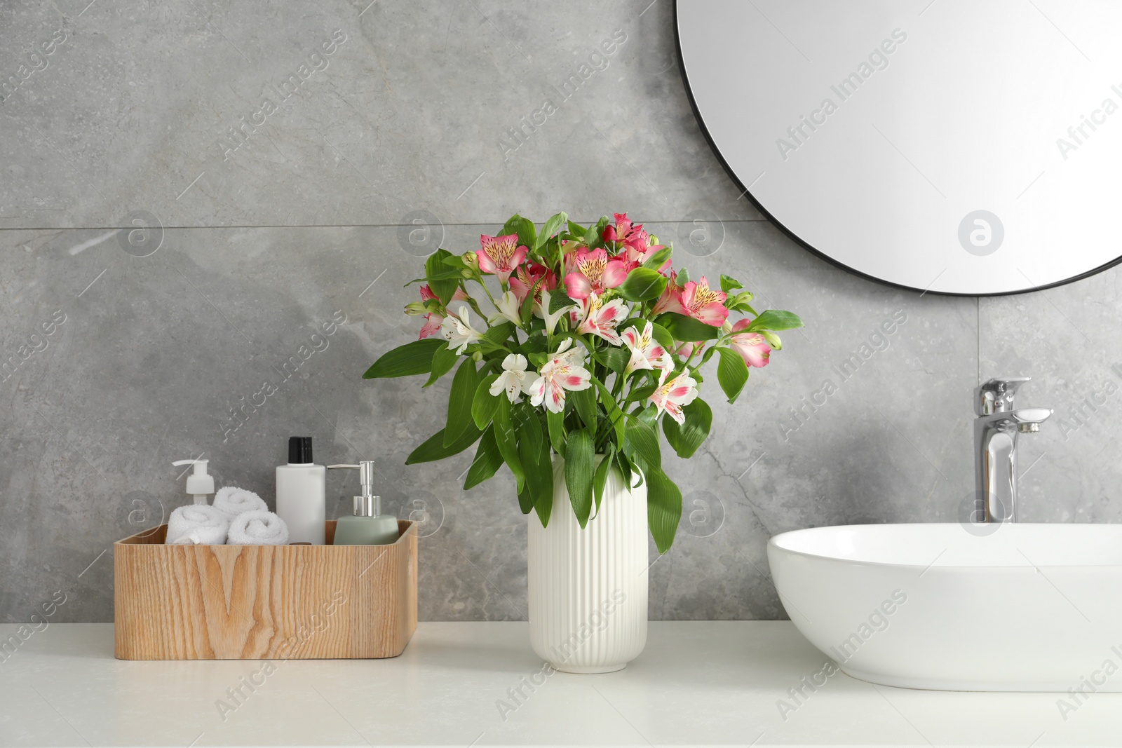 Photo of Vase with beautiful Alstroemeria flowers and toiletries near sink in bathroom