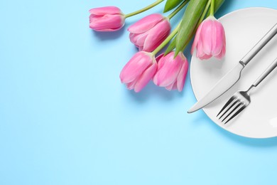 Photo of Stylish table setting with cutlery and tulips on light blue background, flat lay. Space for text