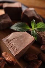Photo of Pieces of tasty milk chocolate, mint and cocoa beans on table, closeup