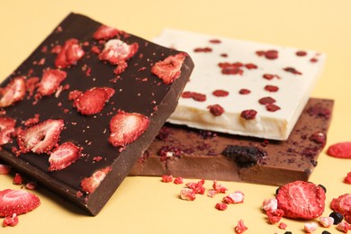 Photo of Different chocolate bars with freeze dried fruits on yellow background