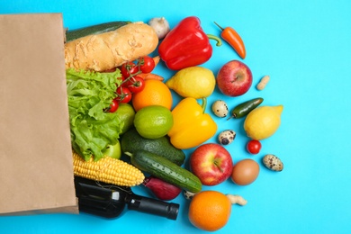 Photo of Paper bag with different groceries on light blue background, flat lay